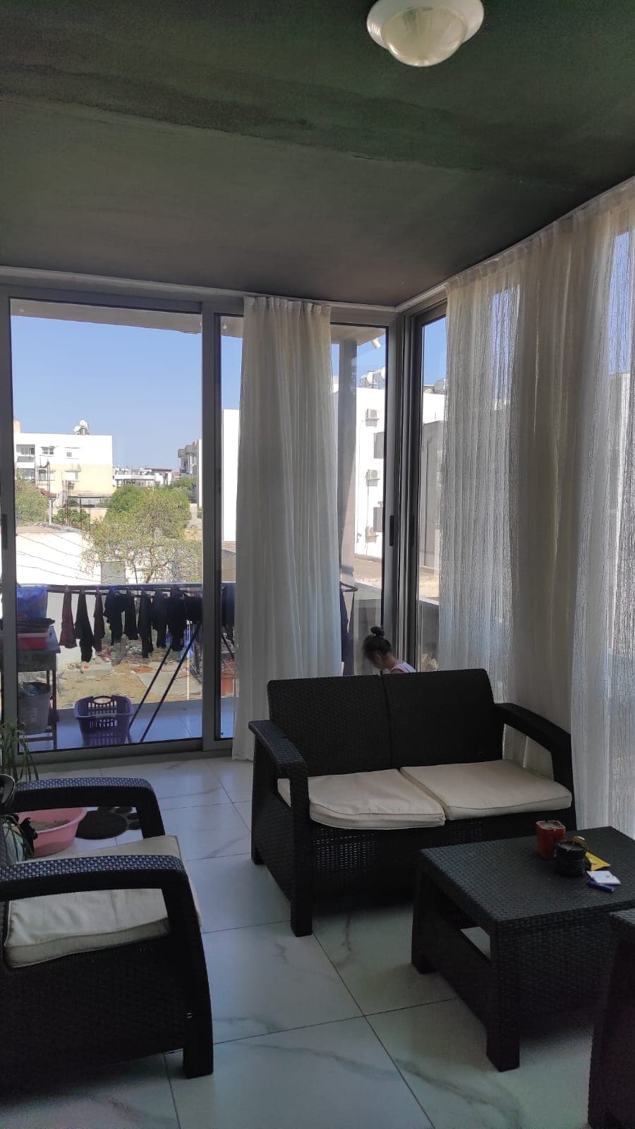 Outdoor seating area and clothes rack on a spacious glass balcony.