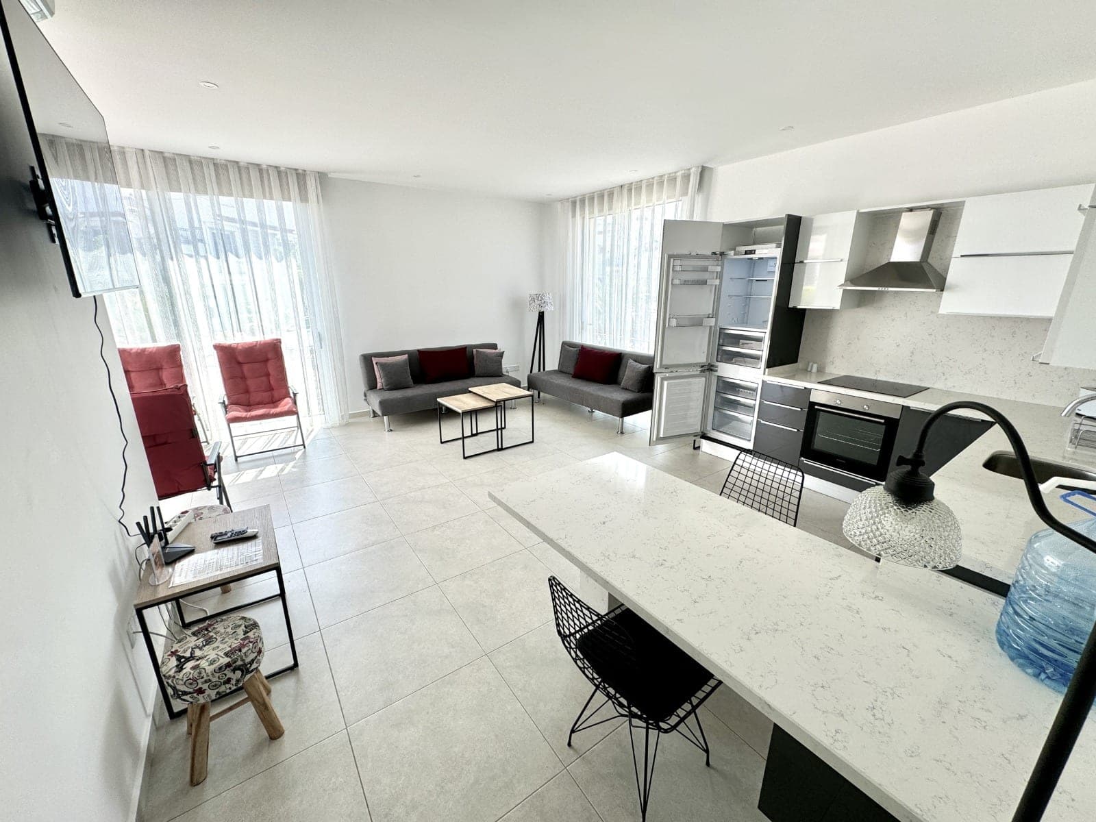 Open-plan living room and kitchen, white tiles and modern furniture.