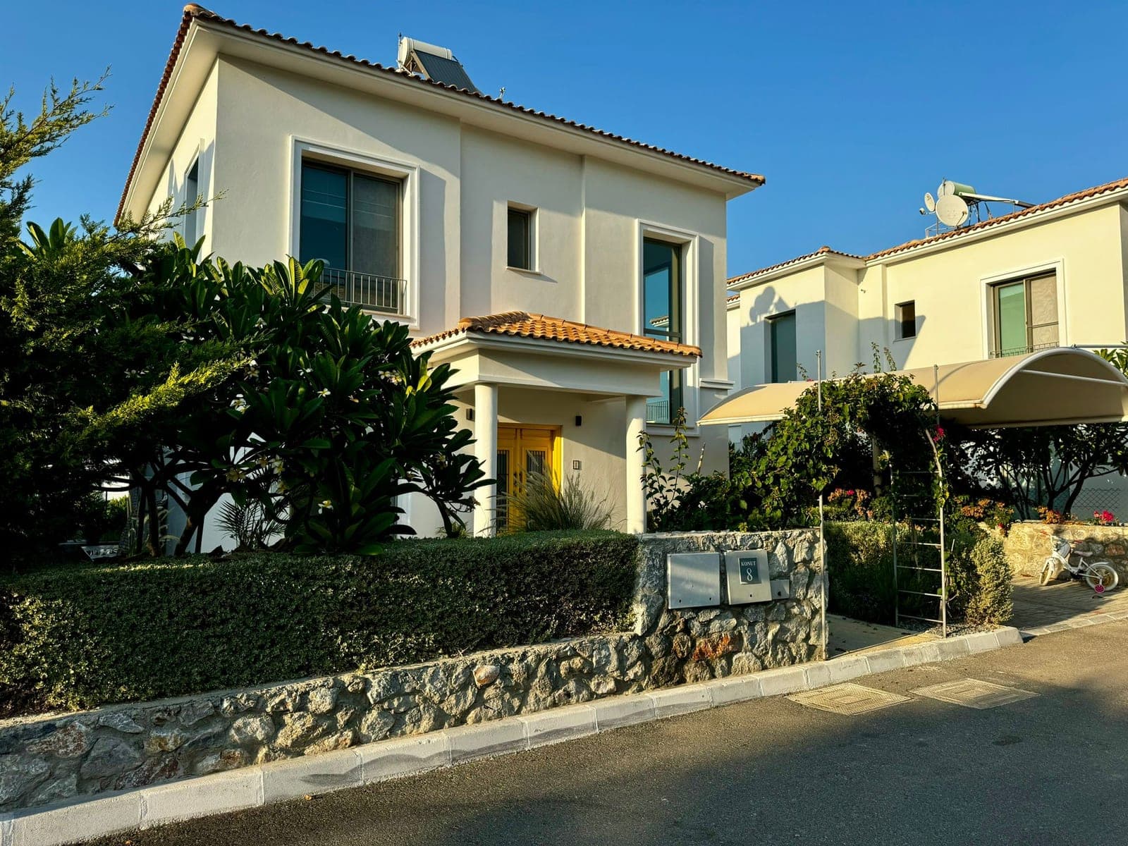 Detached villa with white facade, yellow door, and fenced garden.