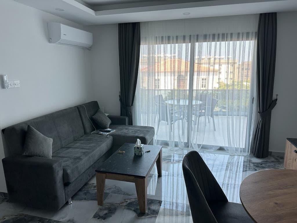 Living room with grey corner sofa, glass door opening to balcony.