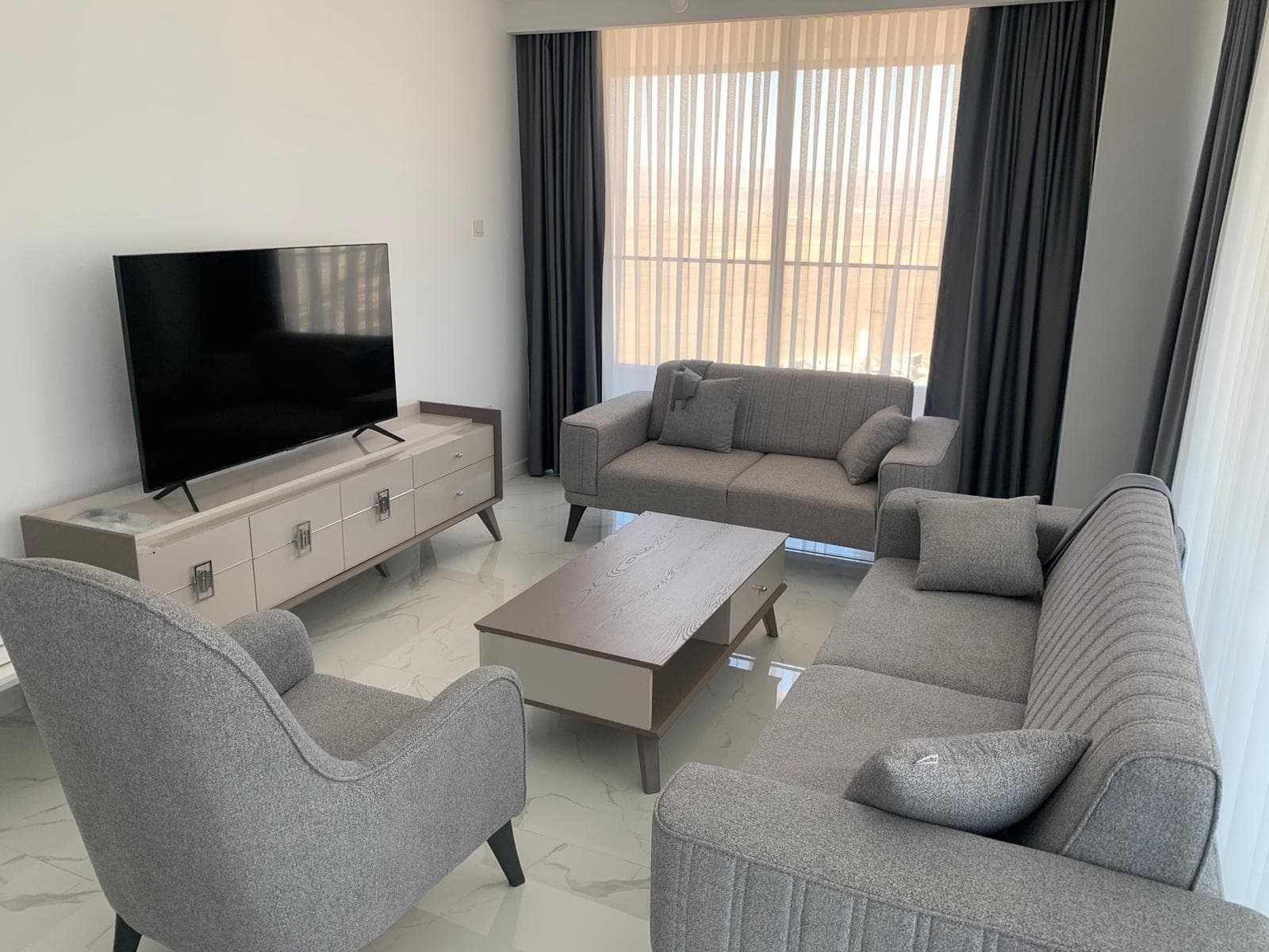 Gri koltuk takımı, sehpa ve TV ünitesi bulunan aydınlık salon.
