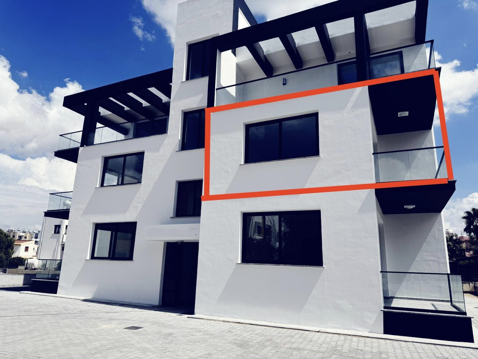Modern designed, white-fronted new apartment building and parking area.