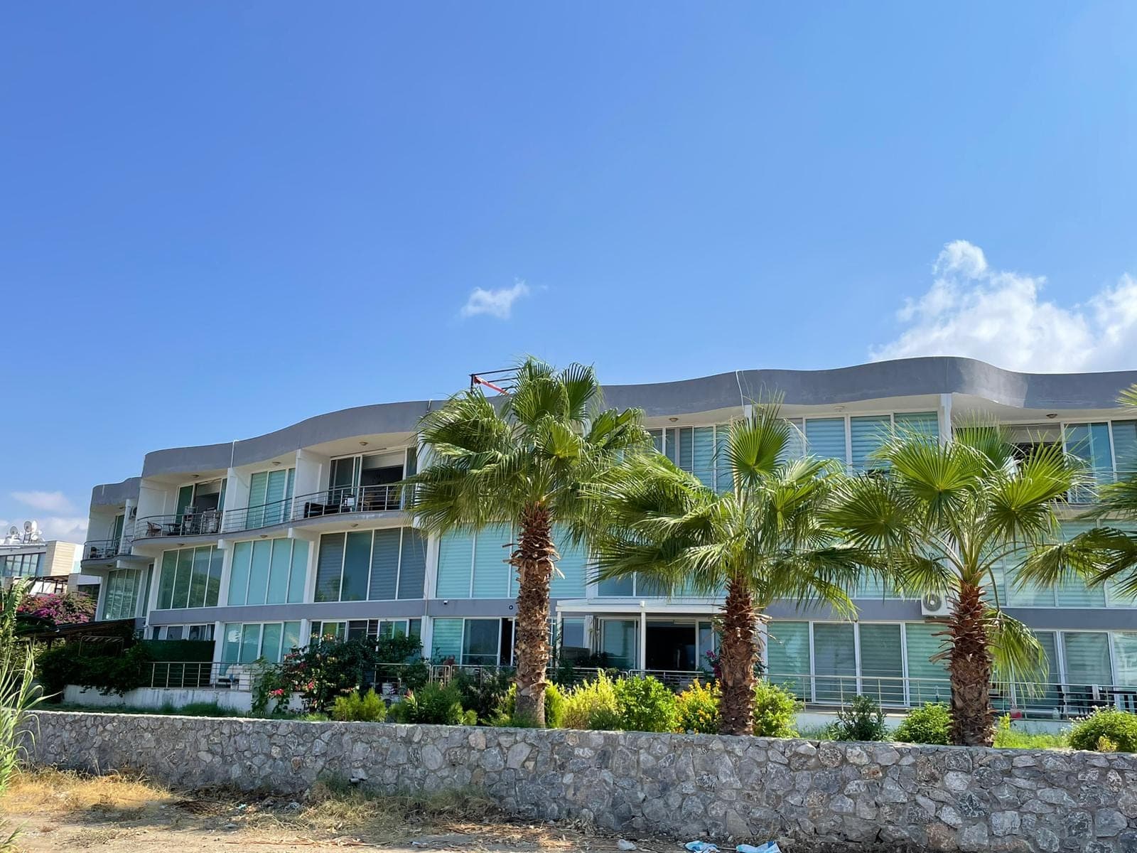 Exterior of an apartment building with modern architecture, in front of palm trees.