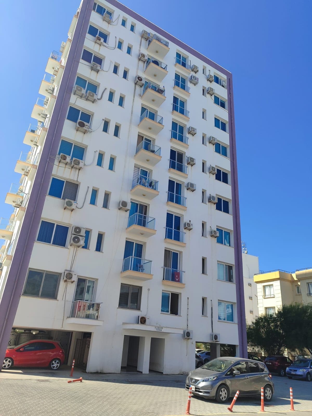 Mor detaylı, çok katlı apartman binasının dış cephesi ve otopark alanı.