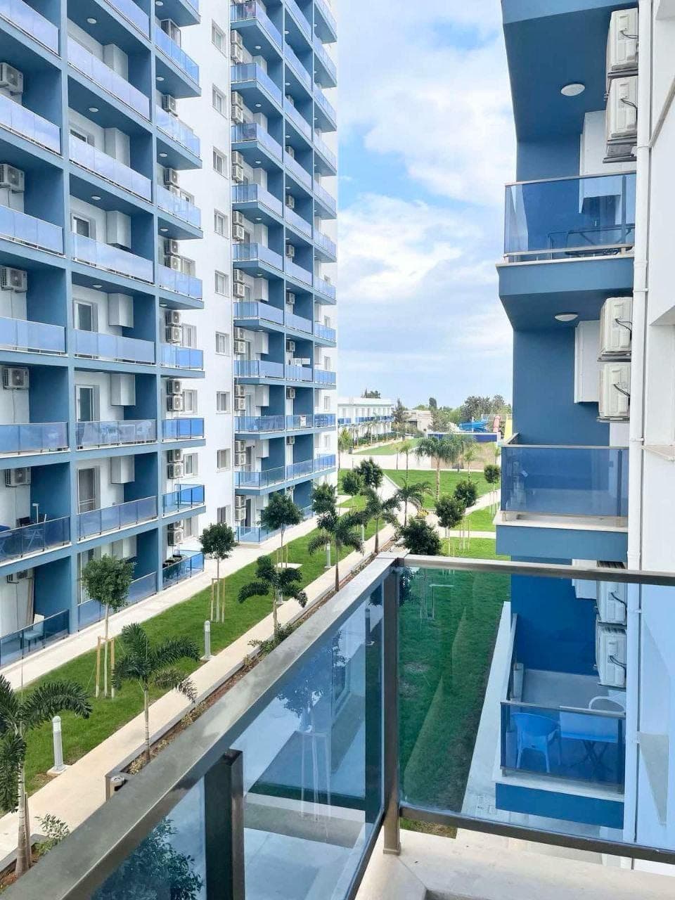 Mavi ve beyaz cepheli apartman binaları, yeşil bahçe ve balkonlar.