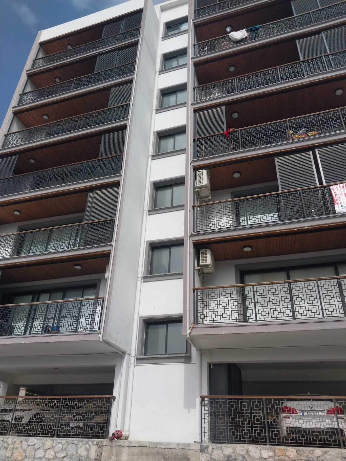 Multi-story building exterior with balconies and ground floor parking area.