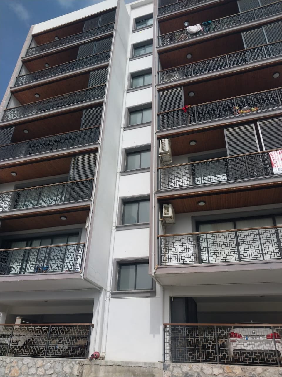 Çok katlı binanın balkonlu dış cephesi ve zemin kat otopark alanı.