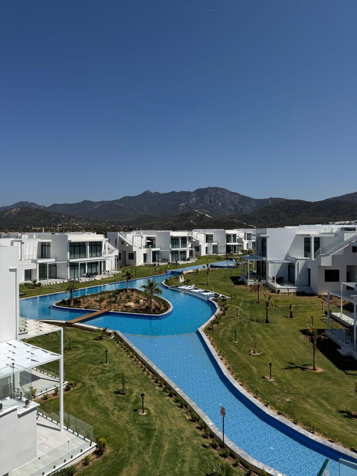 Modern buildings, long pool, green areas and mountain view.