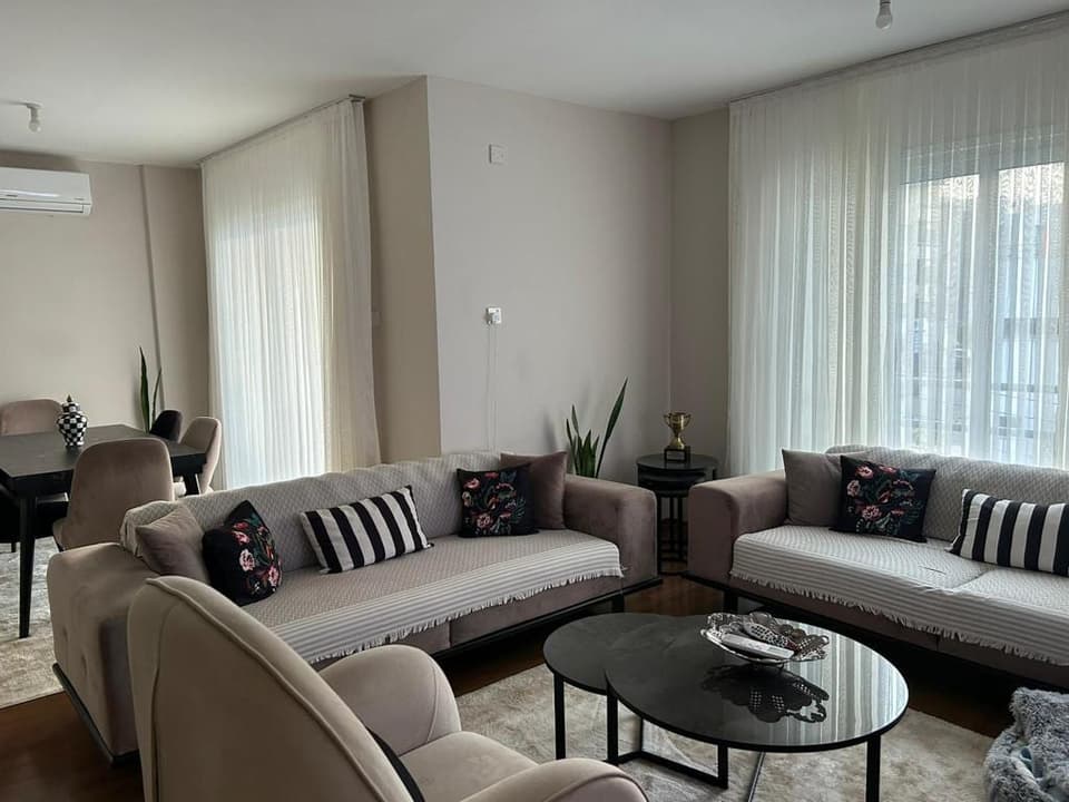 Geniş salon ve yemek alanı, açık renk perdeler ve klima ünitesi.