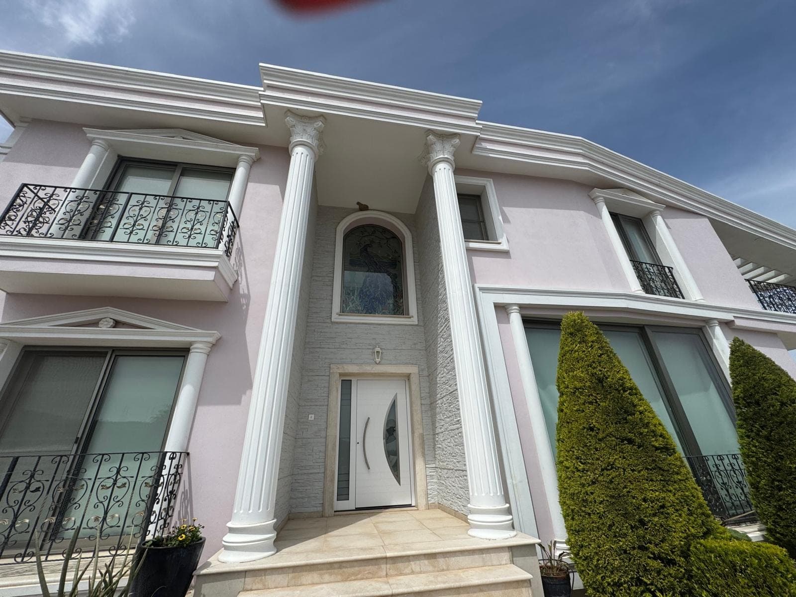 Beyaz sütunlu, pembe cepheli villanın ana girişi ve balkonları