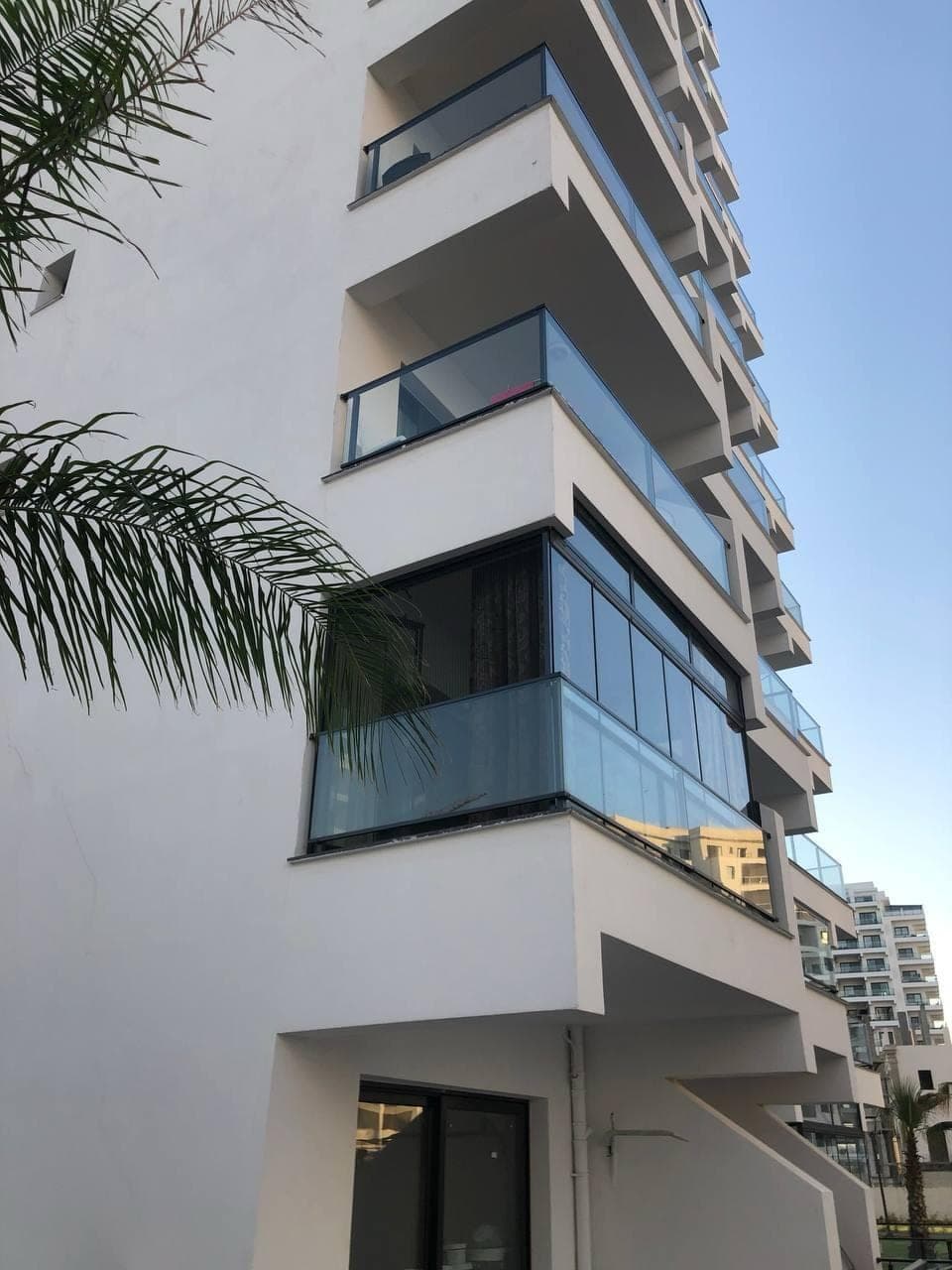 Modern apartman binasının cam balkonlu dış cephesi ve palmiye ağacı.