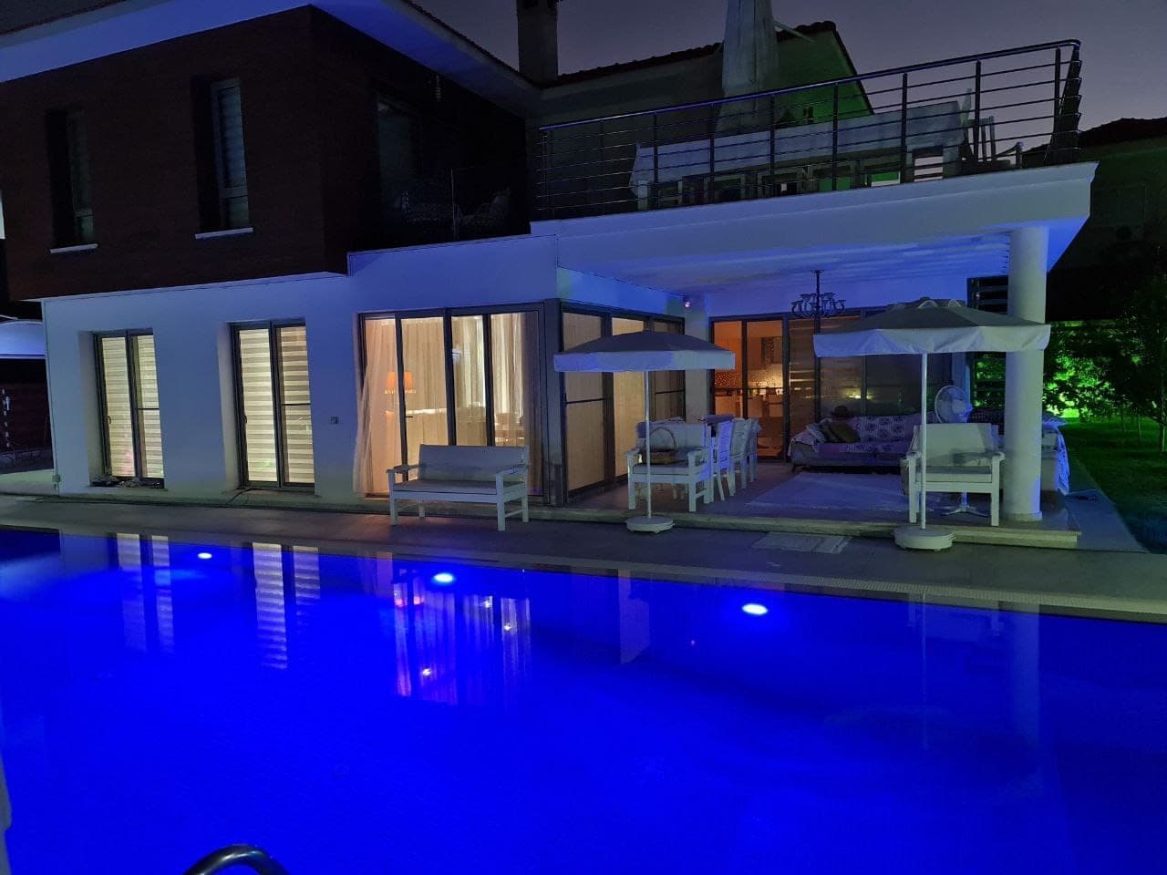 Night view of the villa exterior with illuminated pool and seating area