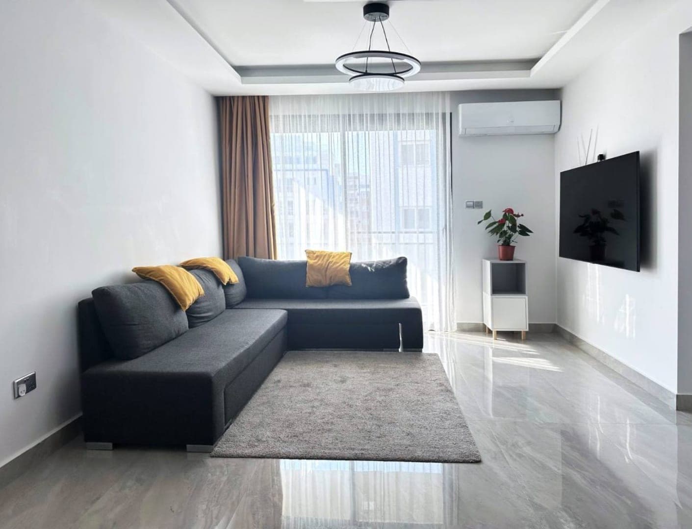 Modern living room with L-shaped sofa and window opening to balcony.