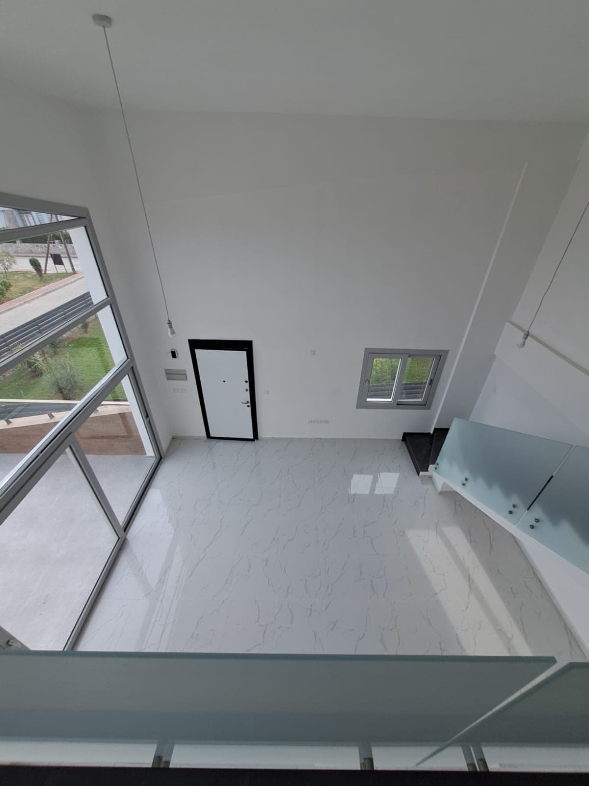 Empty living room with large windows, high ceiling and outdoor view