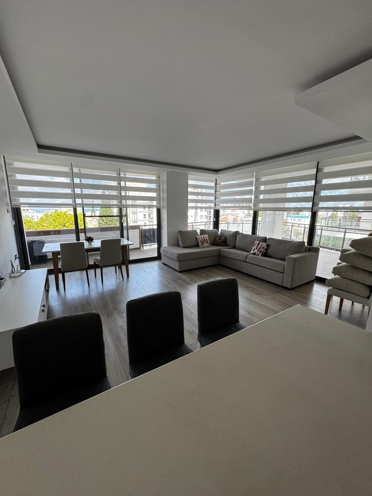 Modern living room with large windows, L-shaped sofa, and dining table.