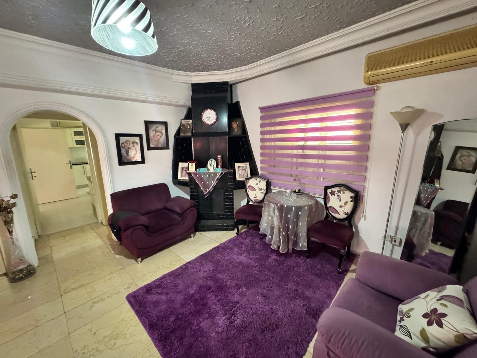Living area decorated with purple rug and sofa set, air conditioner on the wall.