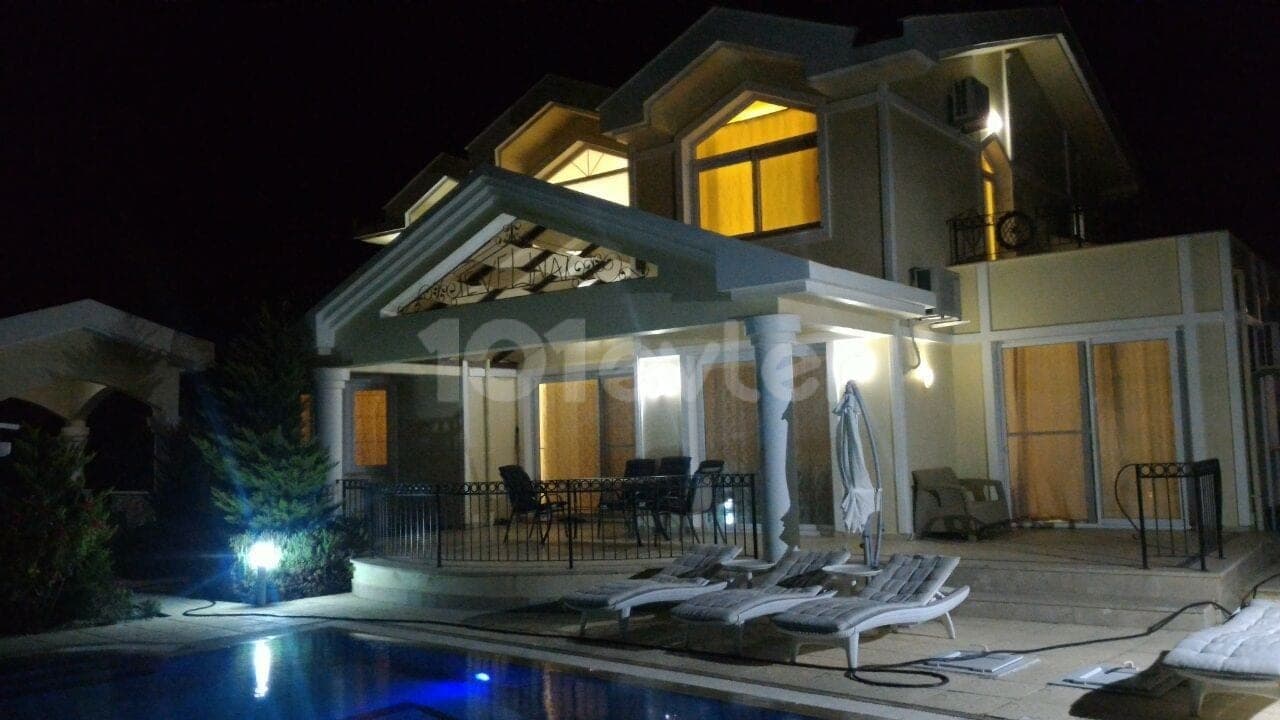 Night view of illuminated pool and villa exterior with seating area