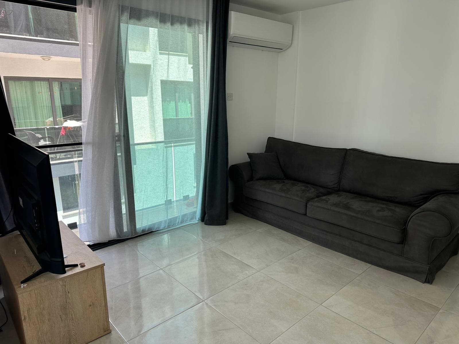 Dark sofa, TV unit, and glass door opening to the balcony