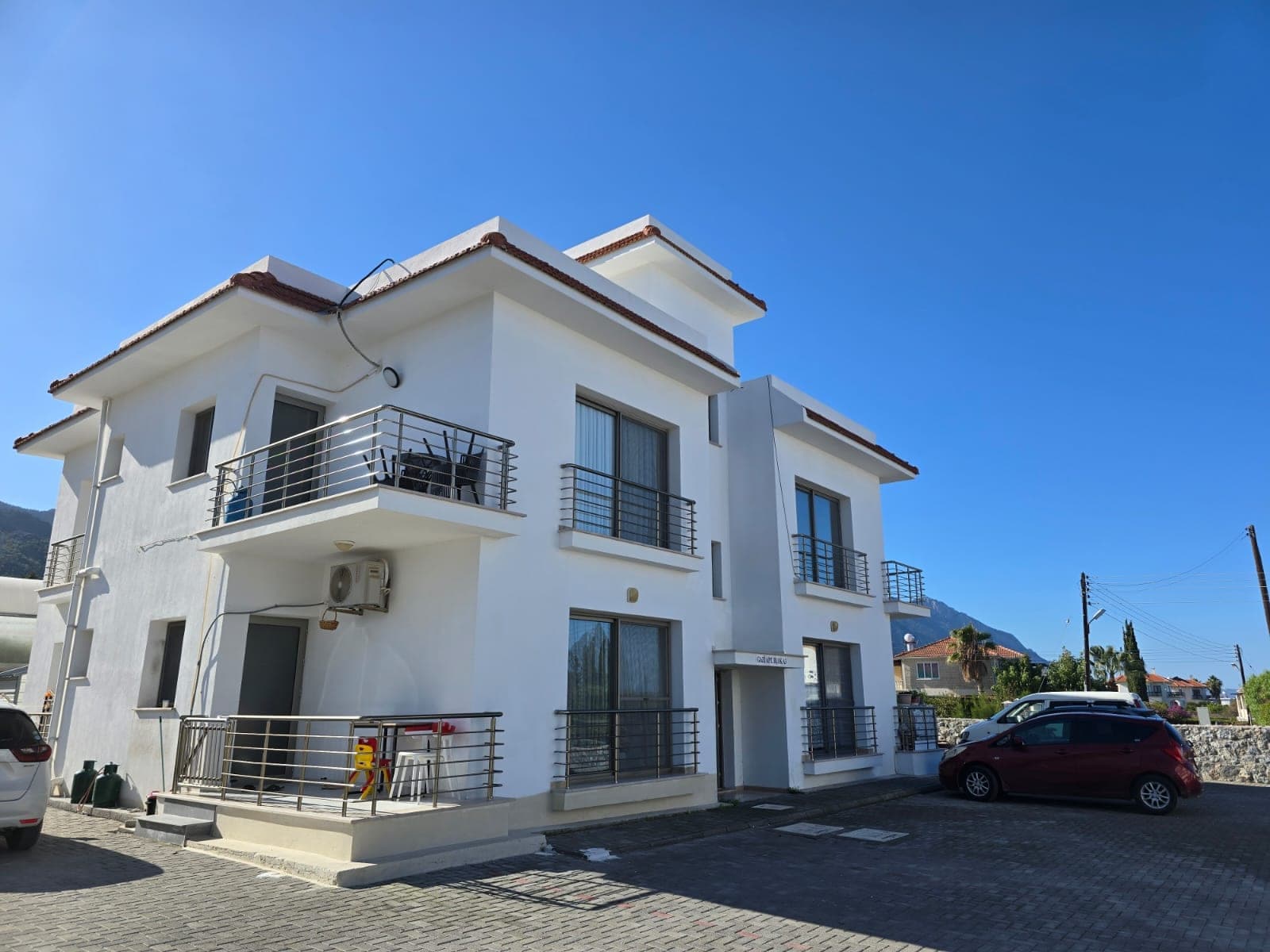 Beyaz cepheli, balkonlu ve otopark alanına sahip apartman binası.