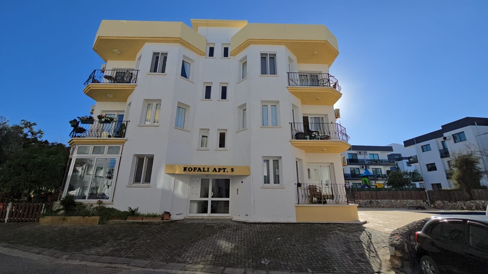 Sarı detaylı beyaz apartman binasının dış cephesi ve otopark alanı.