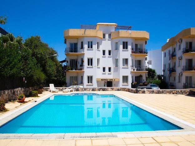 Apartment building with shared swimming pool and parking area in front.