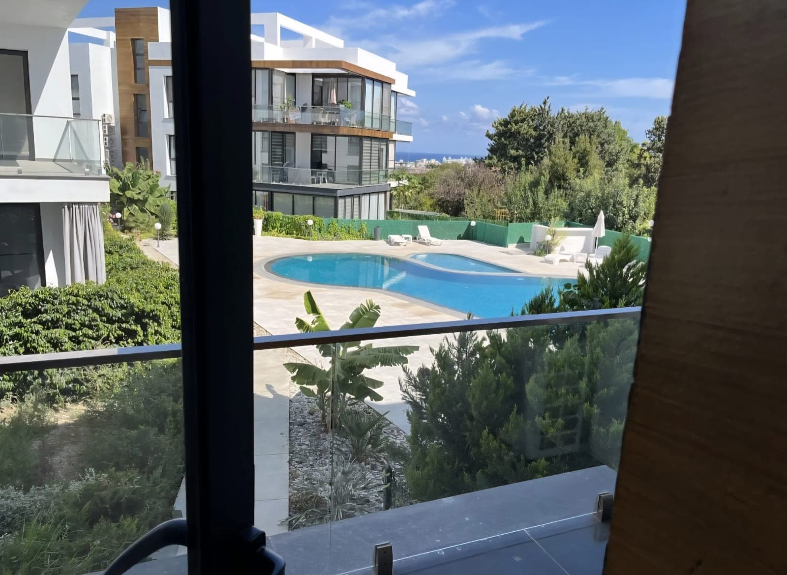 Modern building exterior with pool, garden, and sea view from balcony.