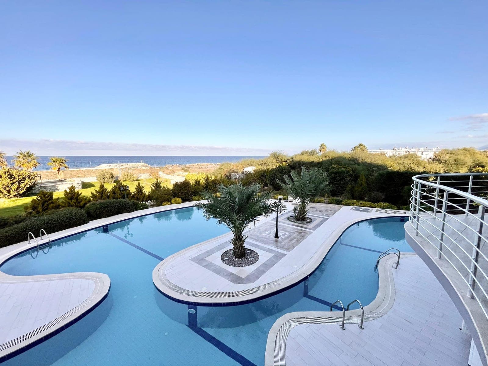 Shared swimming pool with sea view, palm trees and landscaping.