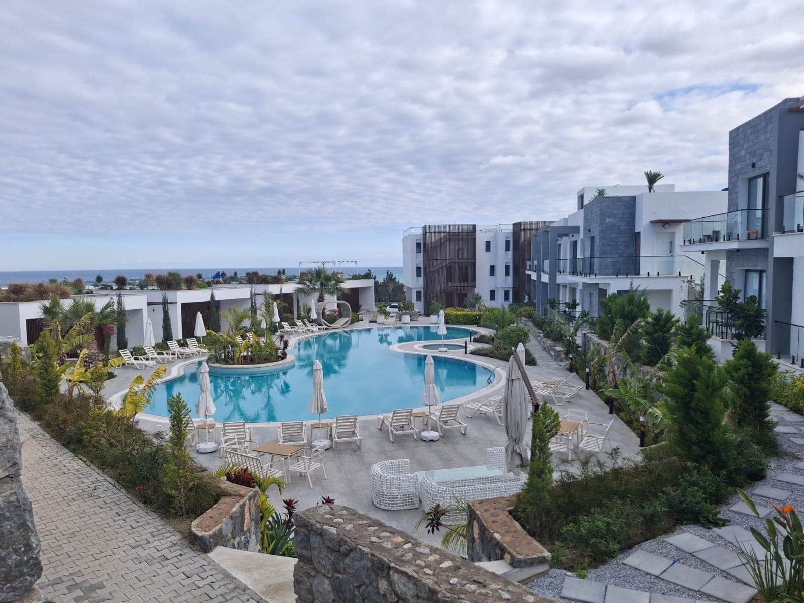 Modern apartment blocks within a complex with a pool and sea view.