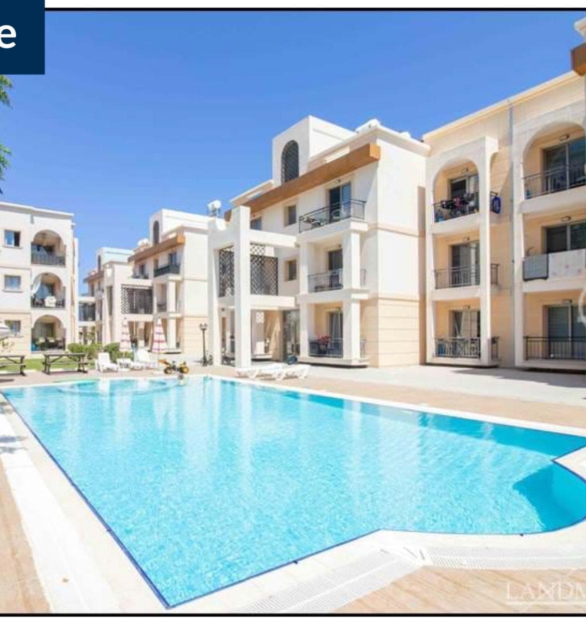 Large shared swimming pool and sunbathing area in front of apartment blocks.