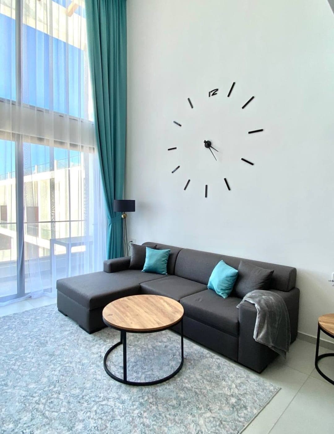 Bright living room with large windows, modern clock, and L-shaped sofa.