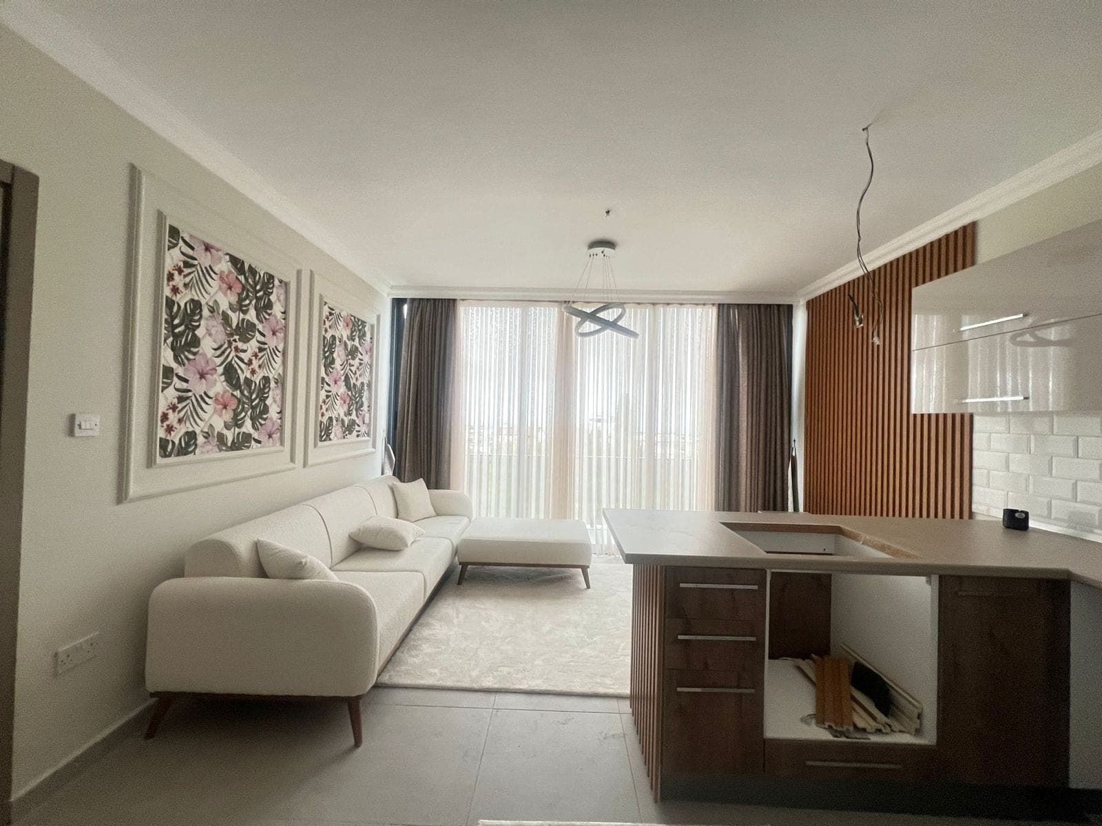 Modern open-plan living room, kitchen, and large window opening to a balcony.