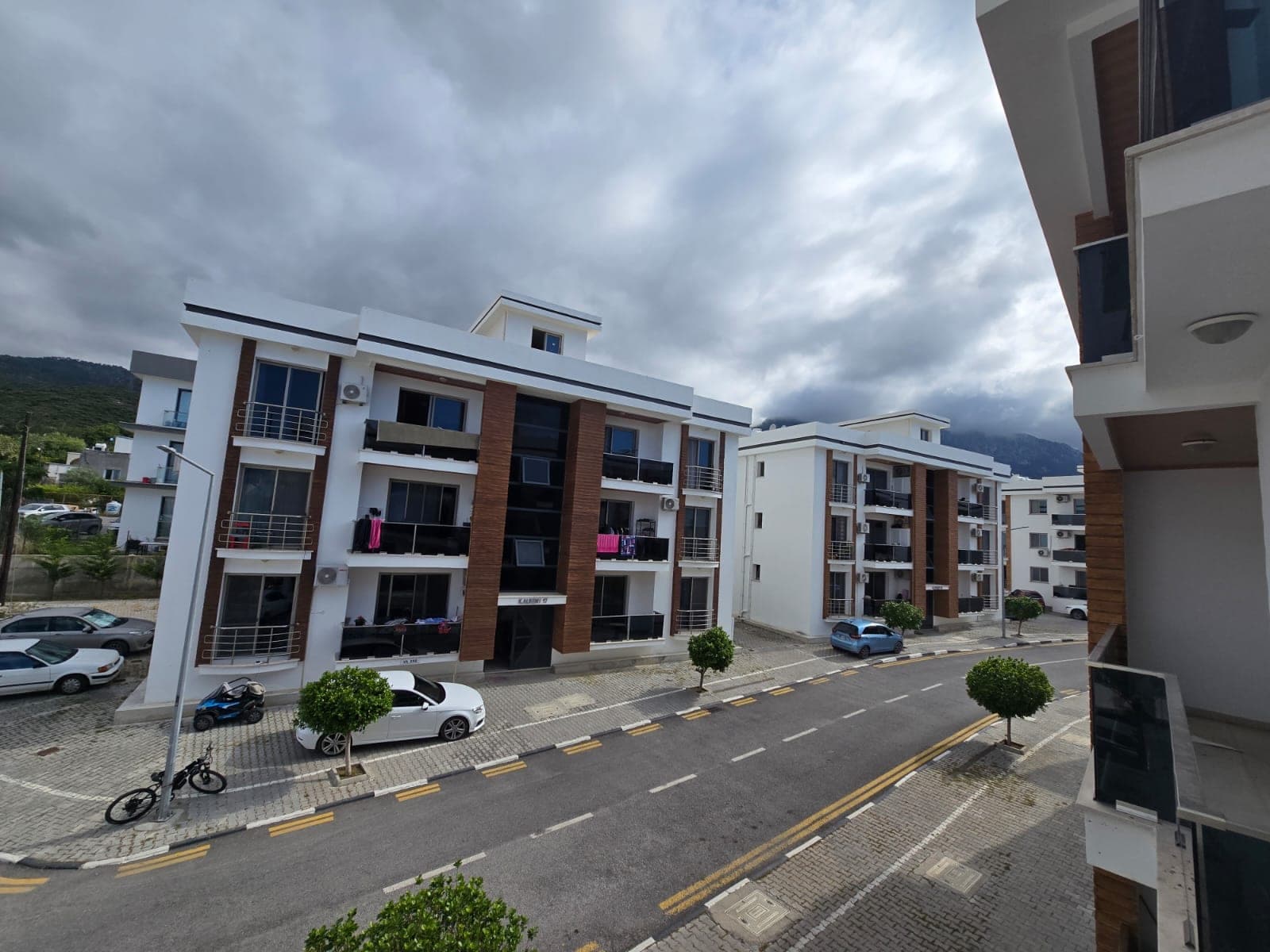 Modern apartman binaları, balkonlar, otopark ve dağ manzarası