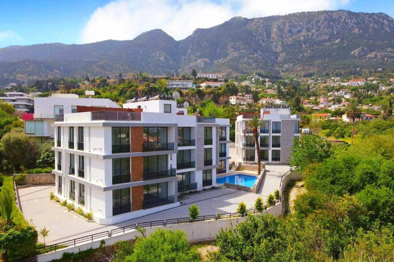 Modern apartment buildings with mountain view, shared pool and parking area.