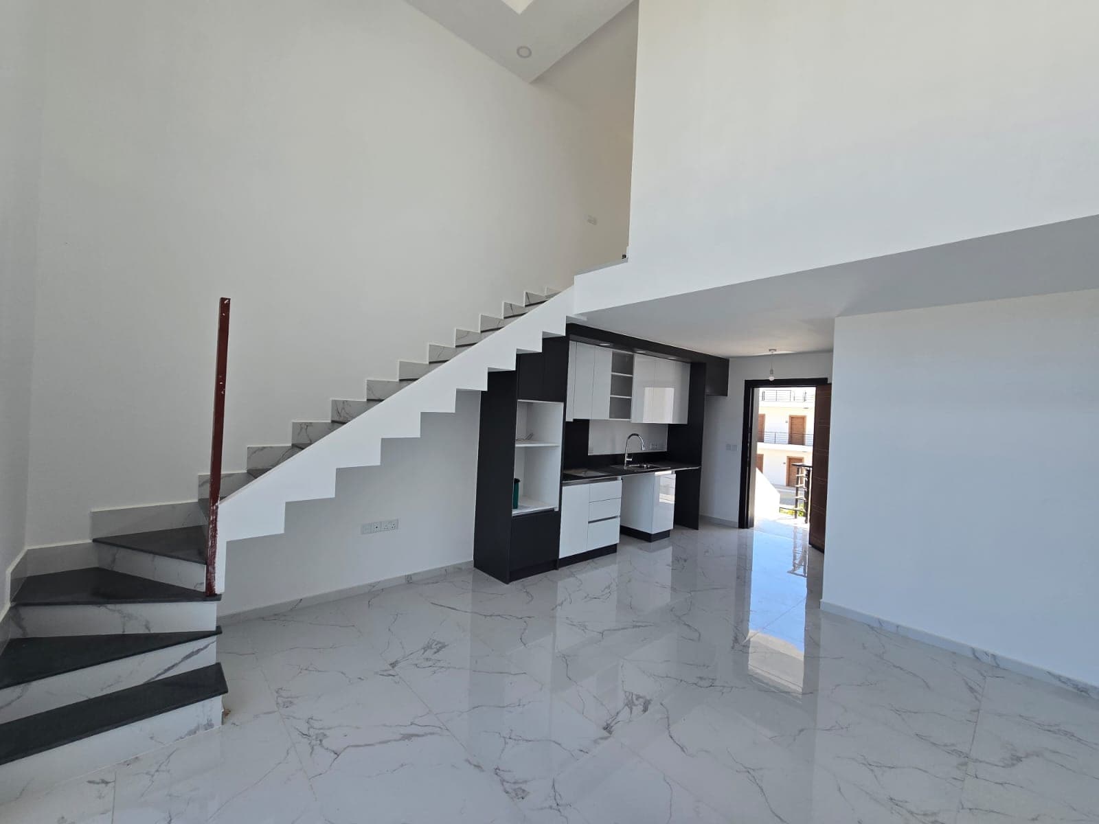 Open-plan living room, kitchen, and staircase area with white marble floor.