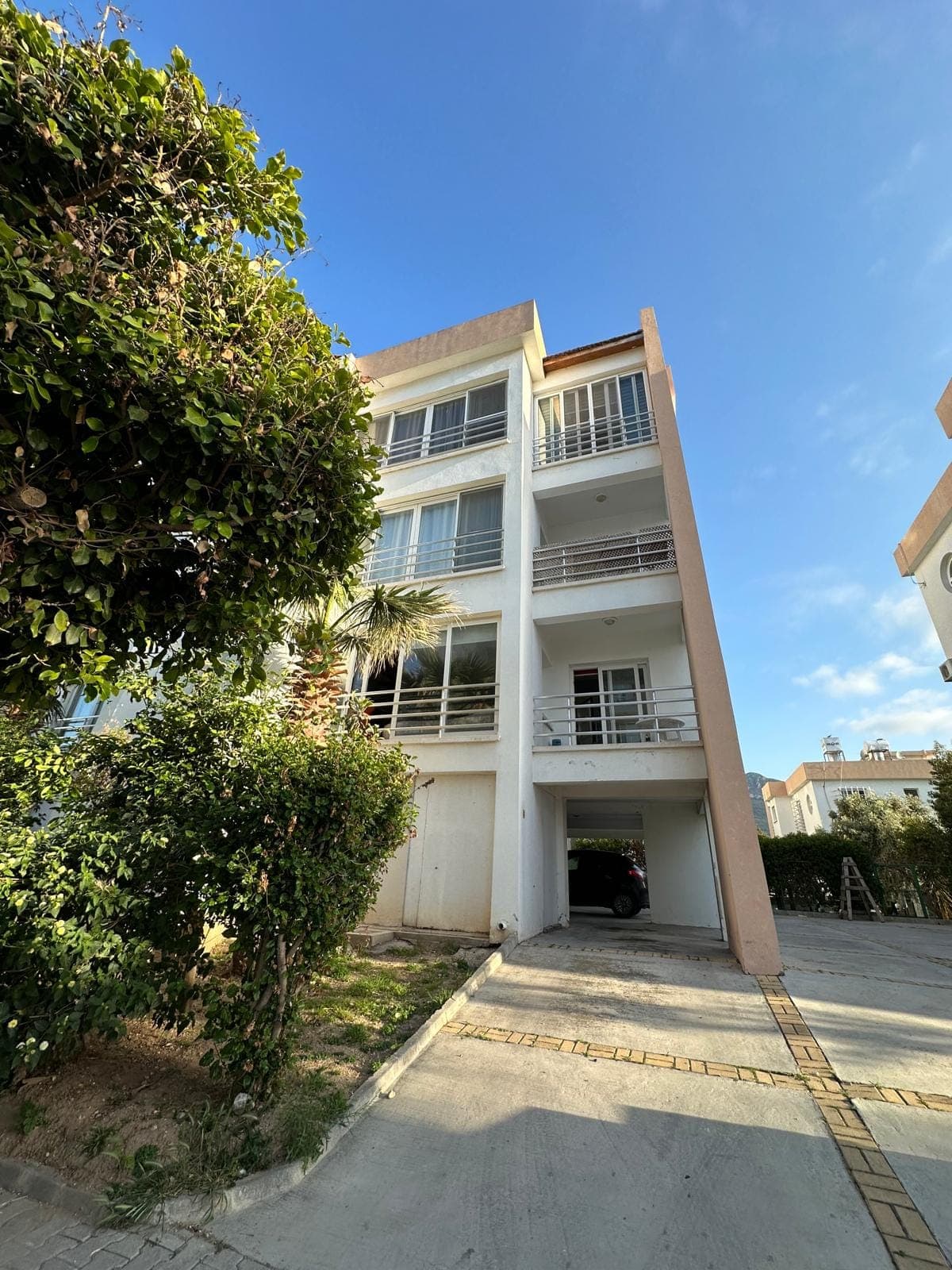 Balkonlu ve kapalı otopark girişli modern apartman binası dış cephesi.