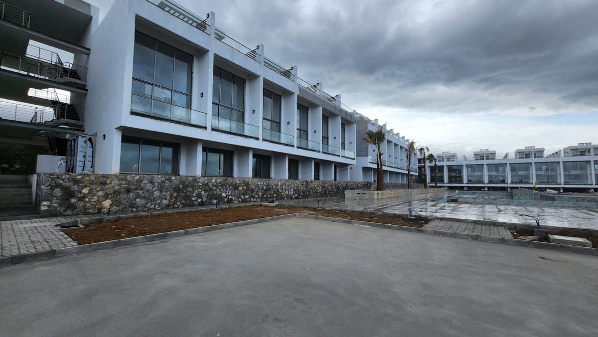 Exterior of modern residences, parking, and pool area under construction.