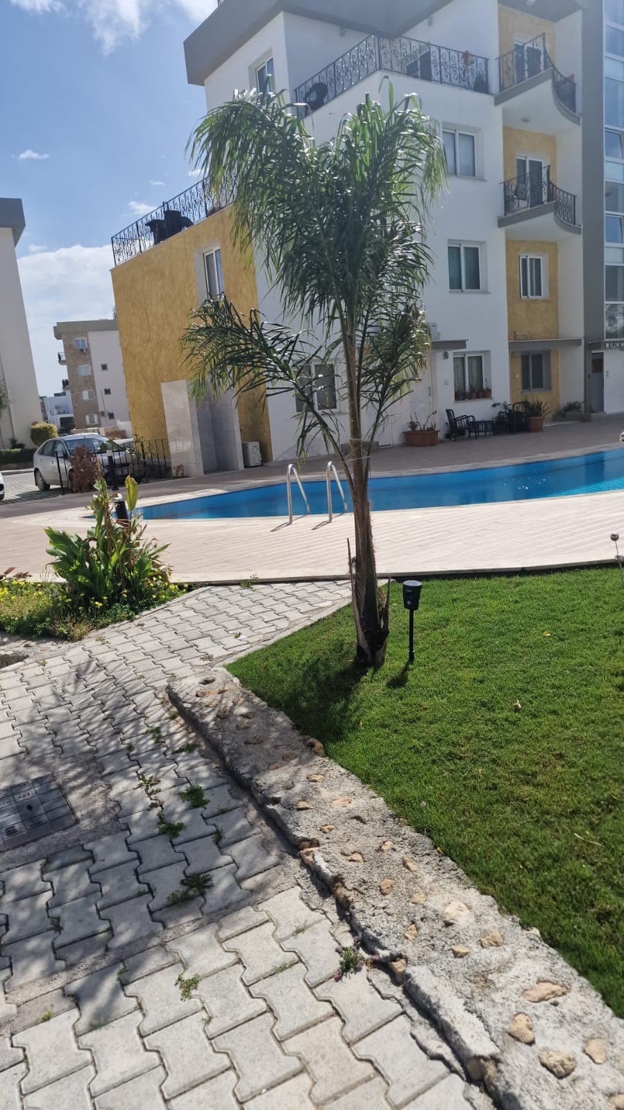 Apartment building exterior with communal pool and green area.