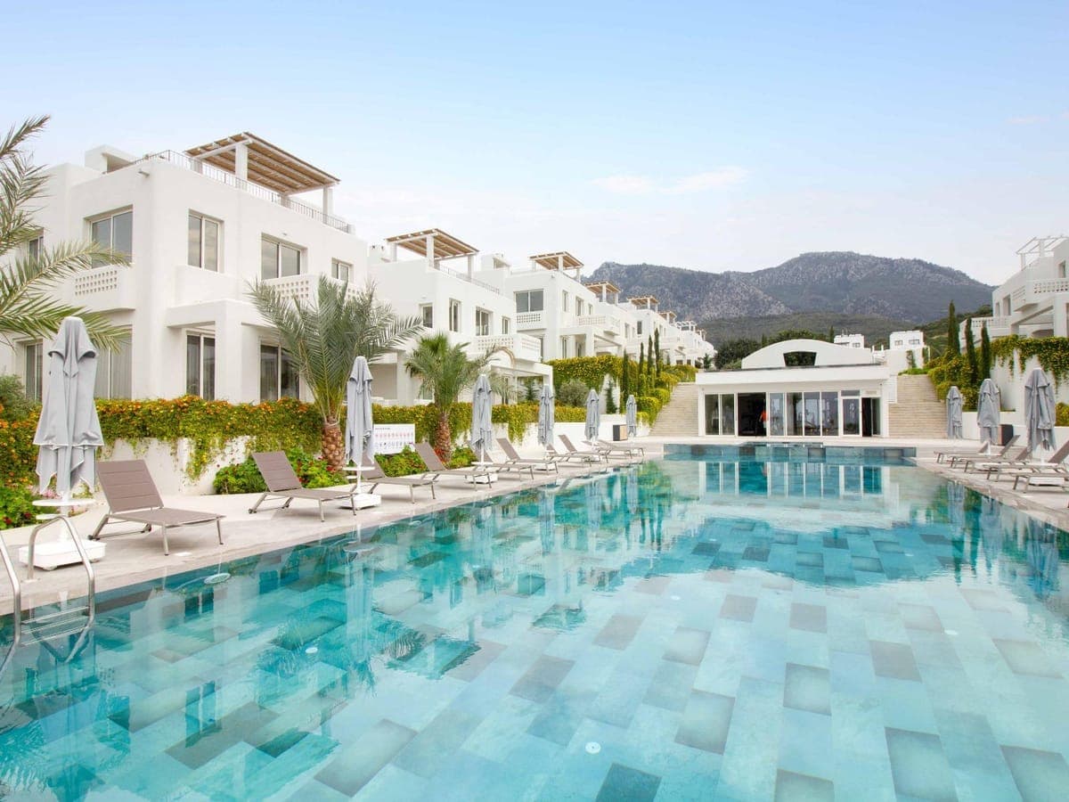 White buildings, large pool area, sun loungers, and mountain view.