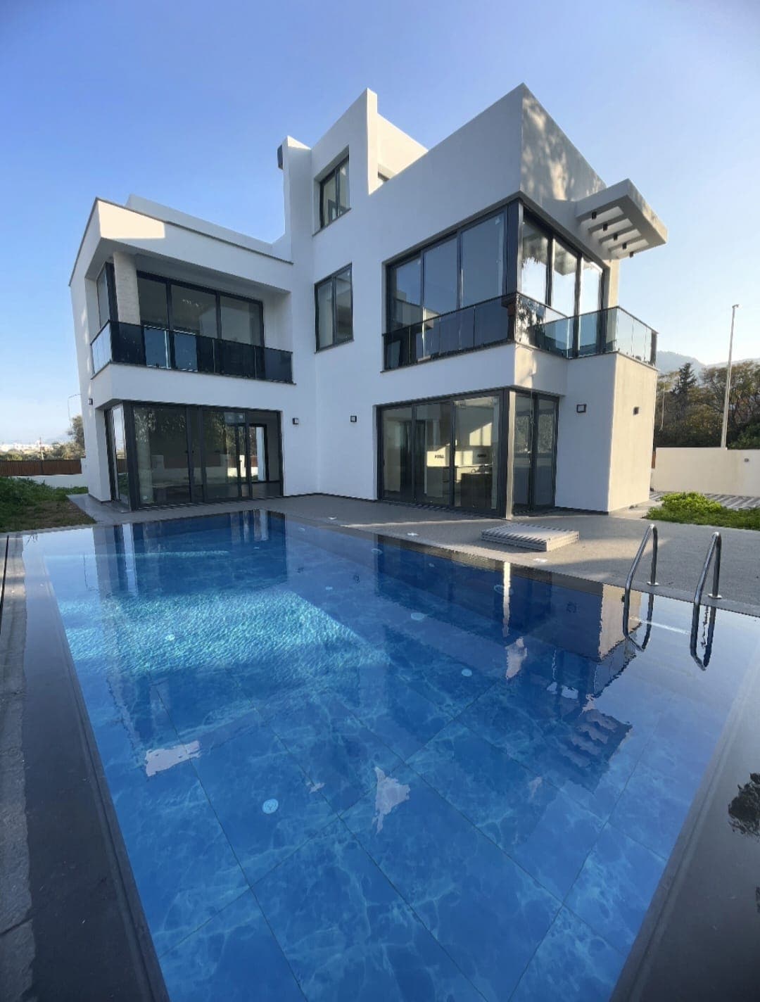 Modern detached house with a rectangular pool in front.