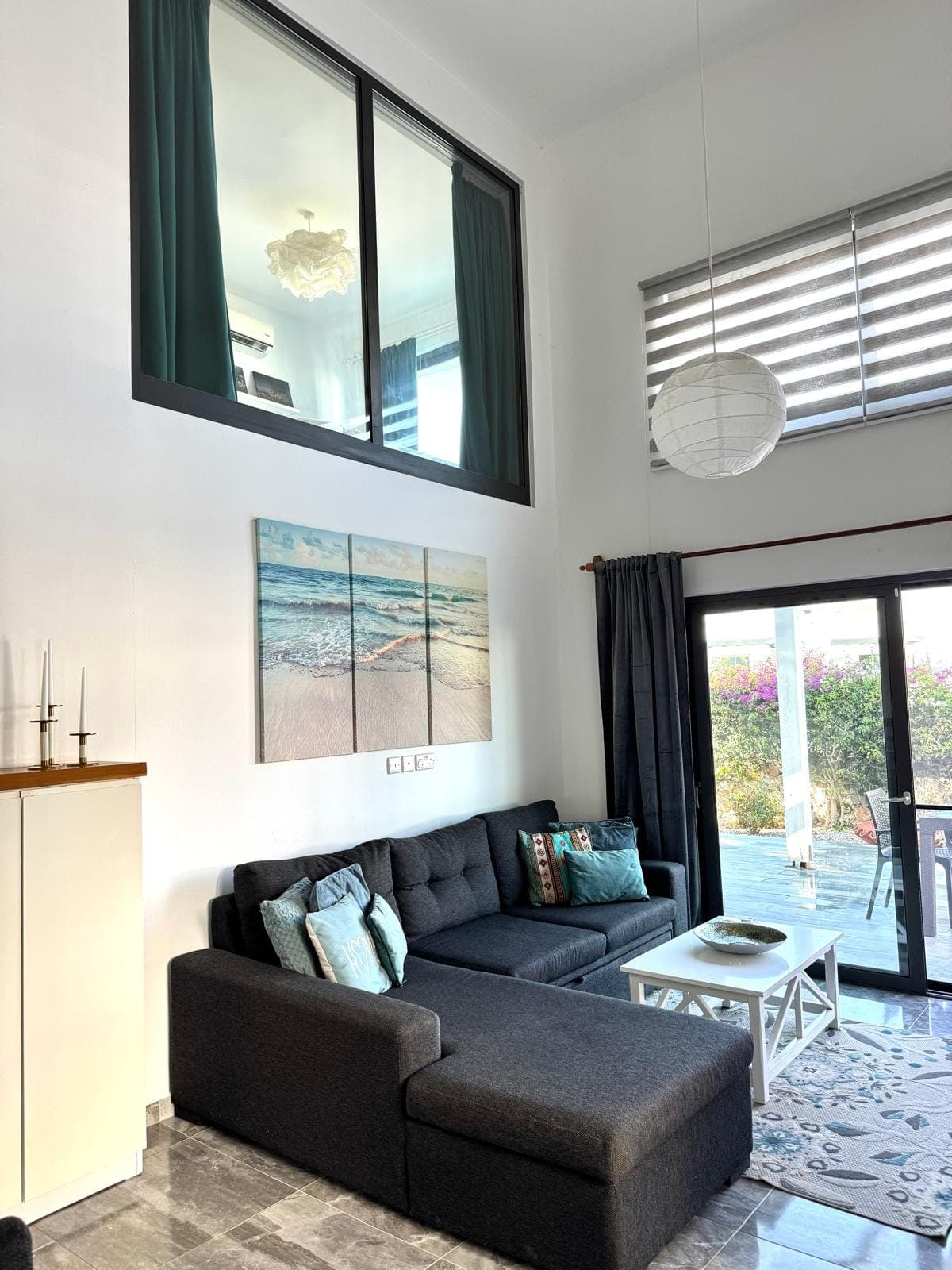 High-ceiling living room with L-shaped sofa, sliding door to garden.