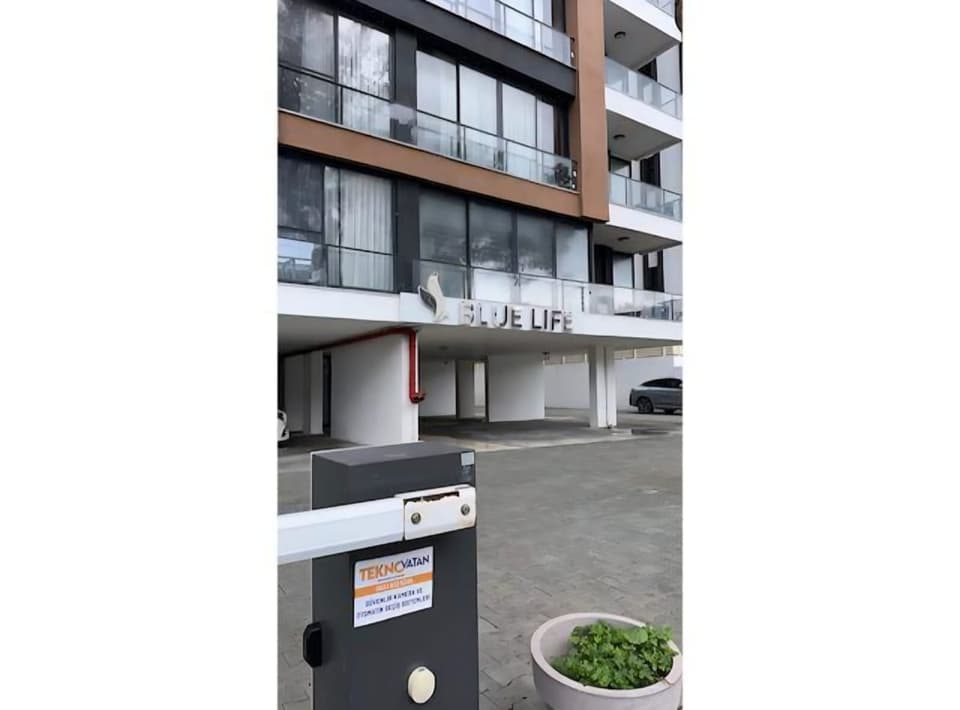 Modern apartman binası girişi ve bariyerli otopark alanı.