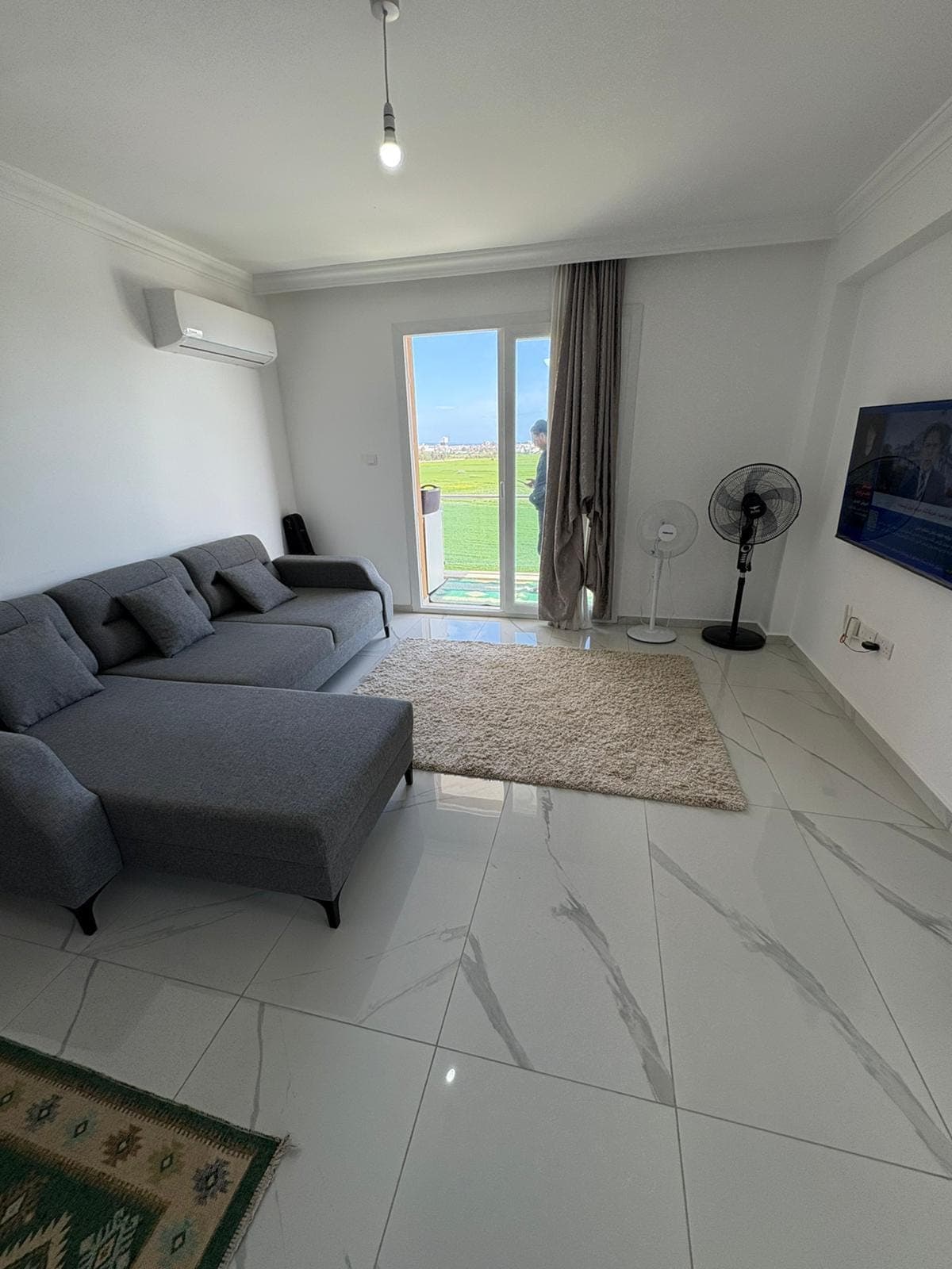 Spacious living room with balcony access and green field view.