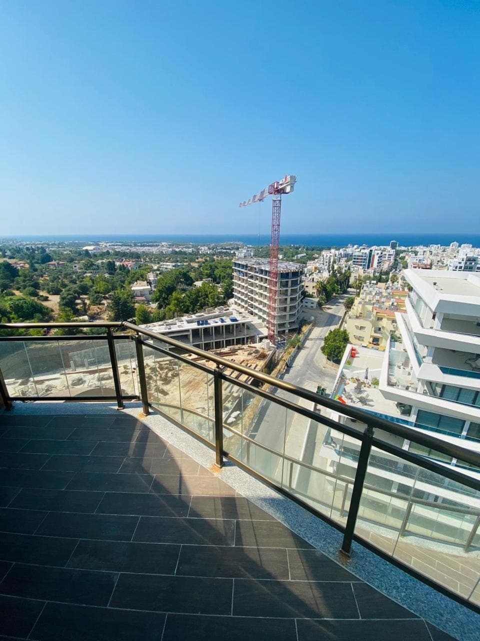 Geniş balkon ve şehir manzarası, uzakta deniz görünüyor.
