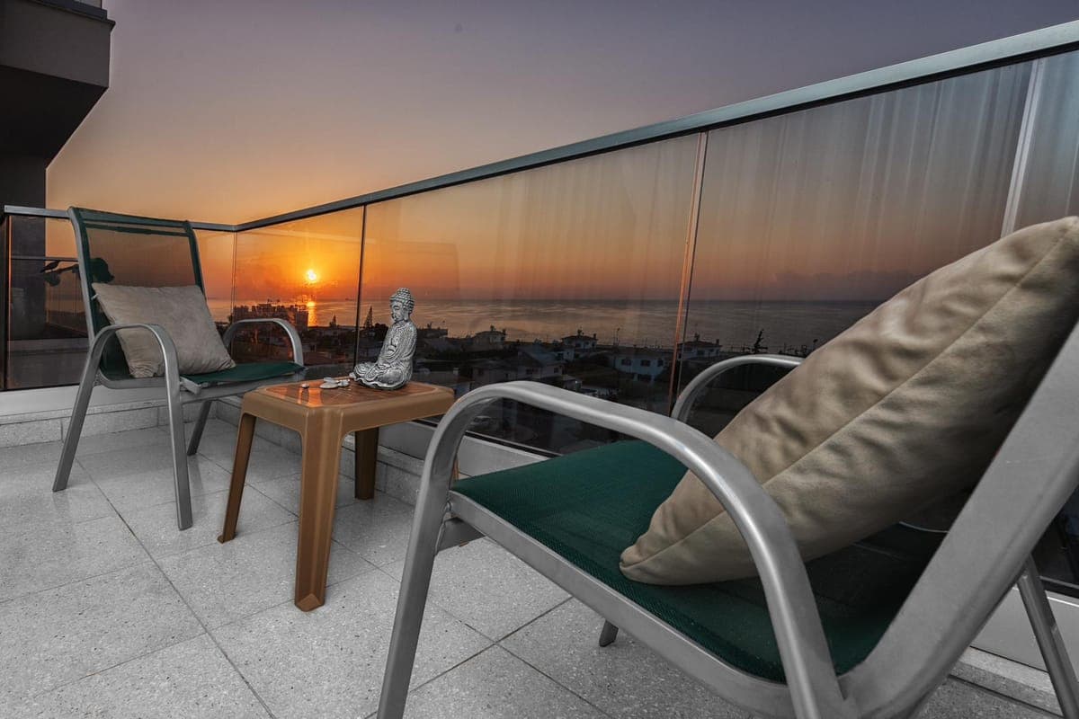 Balcony with seating area and sea view at sunset.