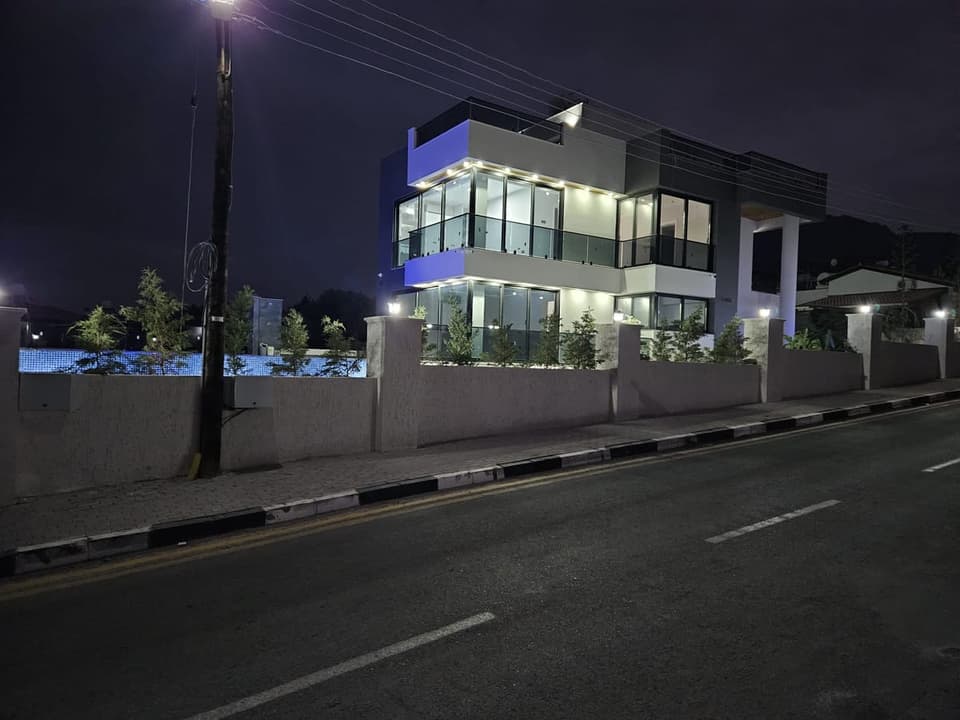 Gece aydınlatmalı modern müstakil evin dış cephesi ve havuz.