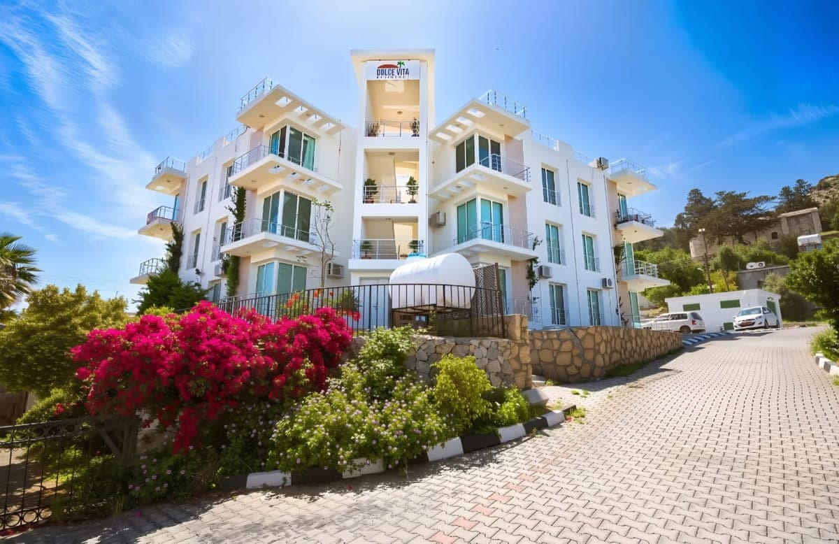 Multi-story building with white facade, 'Dolce Vita' sign, and front garden.