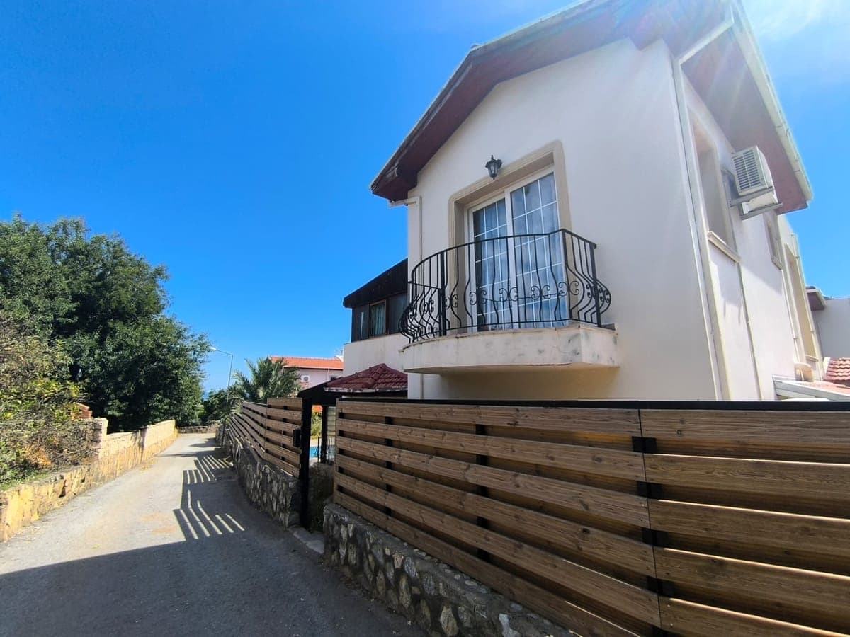 Exterior of a detached house with a balcony and garden fence by the road.