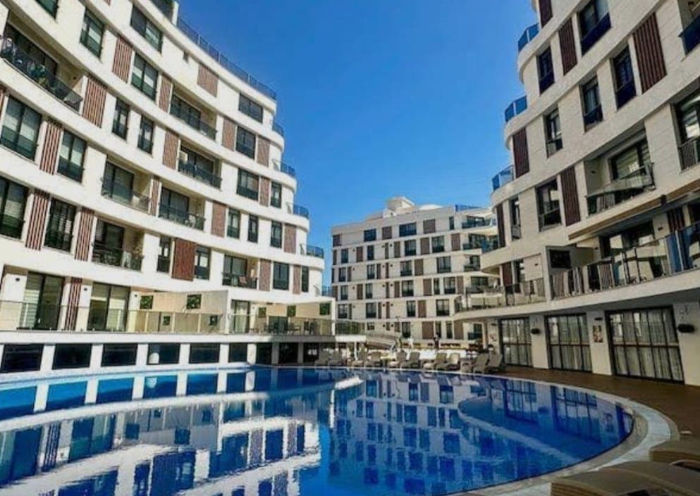 Exterior of a modern apartment complex with pool, under a clear blue sky.