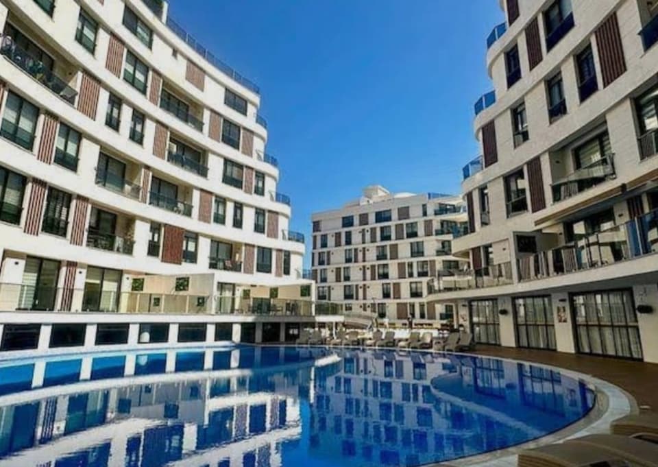 Modern apartman kompleksinin havuzlu dış cephesi, açık mavi gökyüzü.