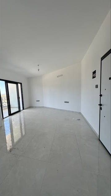Geniş, boş salon alanı ve balkona açılan sürgülü kapılar.